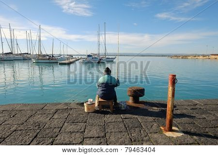 SIRACUSA, ITALY - JENUARY 03: rear view of man sitting and fishing on the Ortigia pier, Old Town of Siracusa. Sicily. Shot in 2015