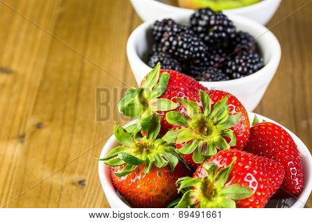Organic fresh fruit in round bowls on wood table.