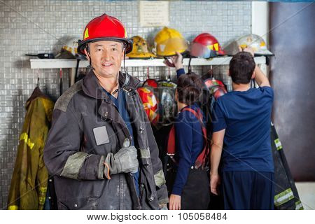 Portrait of smiling mature fireman at fire station with team in background