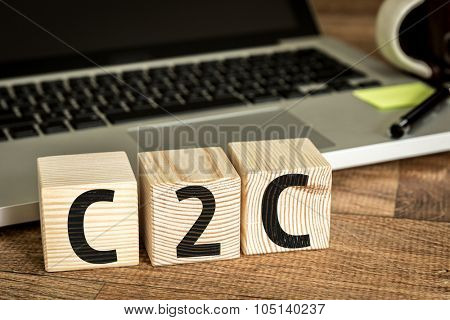 C2C written on a wooden cube in front of a laptop