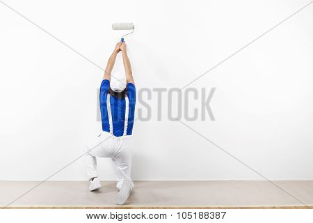 Squatting Painter With Paintroller On White Wall