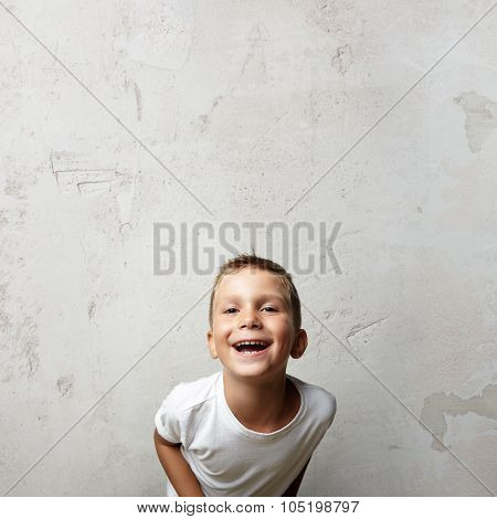 Little cute boy laughing at the camera. Cocrete wall on a background