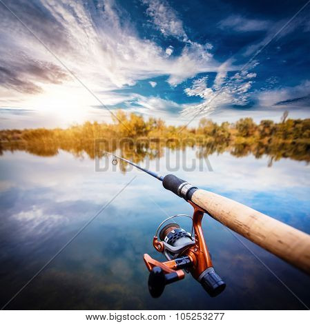 Fishing rod near beautiful pond with cloudly sky