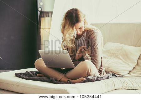 Happy young woman is relaxing on comfortable couch and using laptop at home. Photo toned.