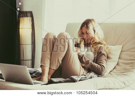 Happy young woman is relaxing on comfortable couch and using laptop at home. Photo toned.