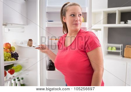 Young female steal piece of chocolate cake from fridge
