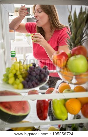 Pretty female sweetens with fresh fruit yogurt from refrigerator