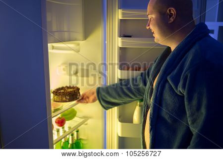 Fat man at night overstep and take whole chocolate cake from refrigerator