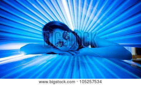 Attractive young woman tanning in solarium and smiling.