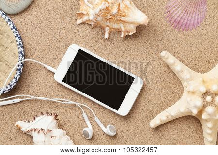 Smartphone on sea sand with starfish and shells. Top view with copy space