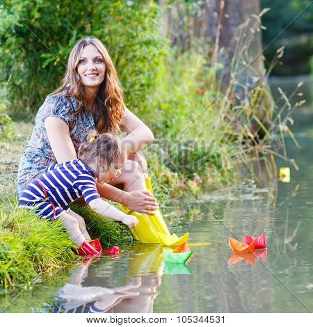 Adorable Little Girl And Her Mom Playing With Paper Boats In A River.