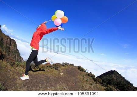 Cheering Young Woman Running On Mountain Peak With Colorful Balloons