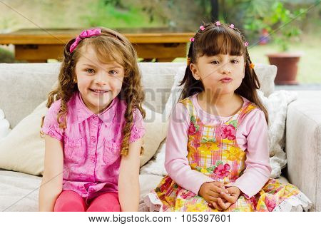 Brunette children sisters sitting happily on white livingroom sofa posing for camera with typical pi