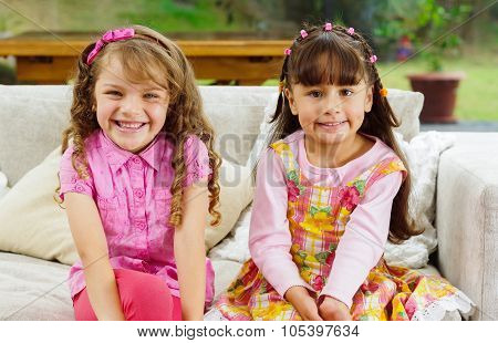 Brunette children sisters sitting happily on white livingroom sofa posing for camera with typical pi