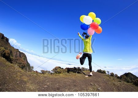 Cheering Young Woman Running On Mountain Peak With Colorful Balloons