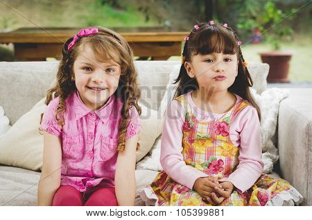 Brunette children sisters sitting happily on white livingroom sofa posing for camera with typical pi
