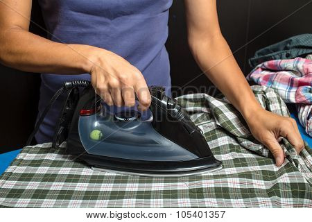 woman in a blue T-shirt ironing plaid shirt and other clothing