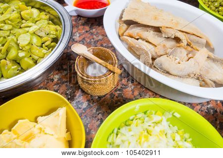 Bowls of different ingredients spread out on granite surface including green peas, onions, abbas, co