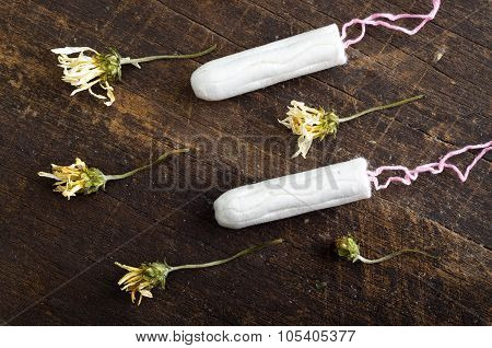 Clean white tampons lying on wooden surface with yellow colored dry flowers around