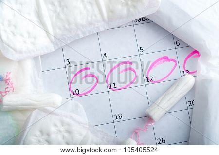 White calendar with pink circles around menstruation date period and clean tampons lying on top