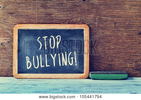 the text stop bullying written with chalk in a chalkboard and an eraser on a blue rustic wooden desk in a classroom