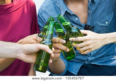 Closeup shot of happy friends toasting with bottles of beer. Girls and guys drinking beer outdoor in a summer day. Close up of female and male hand holding a bottles of beer.