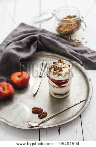 Yogurt oat granola with berries, honey, nuts and nectarins in glass jar on vintage metal tray over r