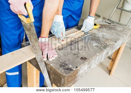 building, carpentry, repair, teamwork and people concept - close up of builders with arm saw sawing board on table