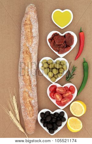 French baguette bread loaf with antipasti selection of fresh and sun dried tomatoes, green and black olives, chilli peppers, olive oil and lemon halves.