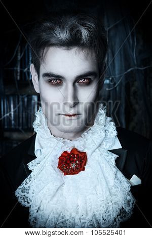 Handsome vampire man wearing elegant tailcoat stands in the old medieval castle. Halloween.