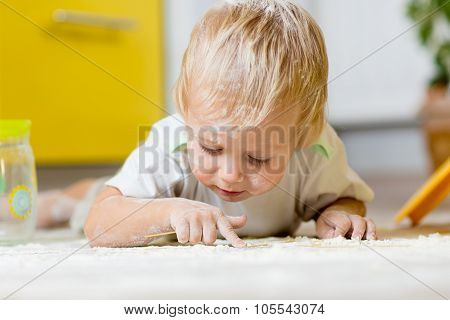 Little child laying on very messy kitchen floor, covered in white baking flour