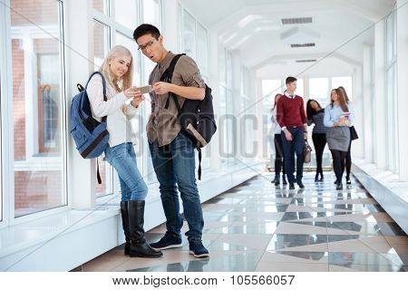 Portrait of a happy students using smartphone in the university hall