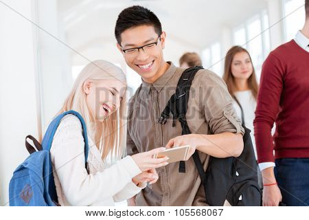 Portrait of a happy man and woman using smartphone in the university hall