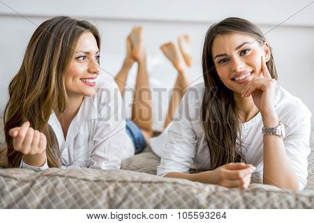 Two Beautiful Girls Talking And Smiling While Lying On A Bed