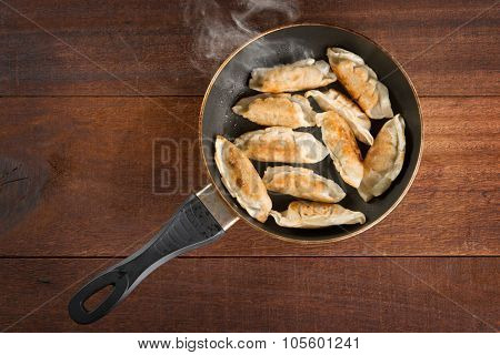 Top view fried dumplings in a frying pan. Chinese food cooking with hot steams, on rustic vintage wooden background. 