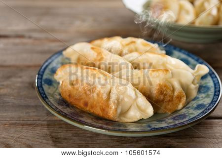 Fresh pan fried dumpling on plate. Chinese dish with hot steams on rustic vintage wooden background. Fractal on the plate is generic print.