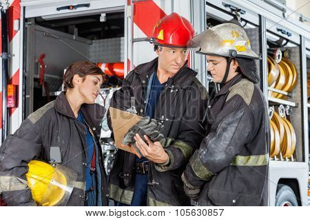 Male firefighter showing clipboard to colleagues against truck at fire station