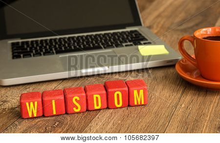 Wisdom written on a wooden cube in front of a laptop