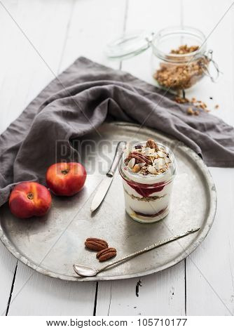 Yogurt oat granola with berries, honey, nuts and nectarins in glass jar on vintage metal tray over r