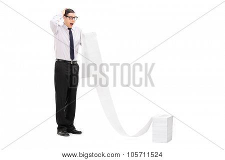 Full length portrait of an upset young businessman reading a long list stacked in front of him isolated on white background