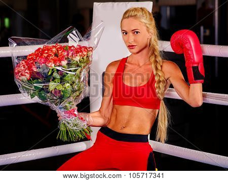 Girl wearing red gloves with bouquet flowers sitting in corner of boxing ring.