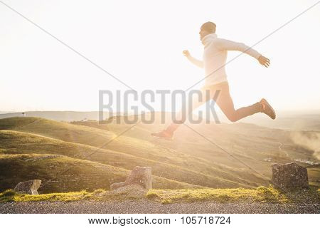 Man jumping over precipice between two stones on mountains at sunset