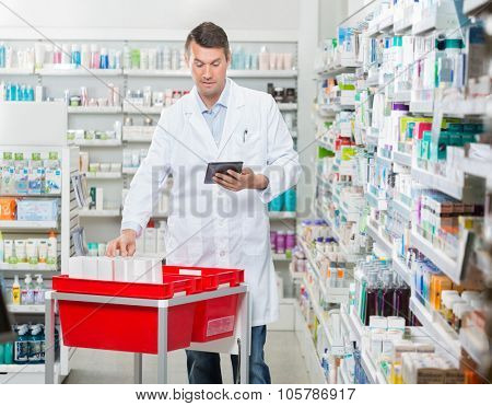 Mid adult male pharmacist counting stock while using digital tablet at drugstore
