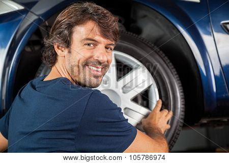 Portrait of happy mechanic fixing hubcap to car tire at garage