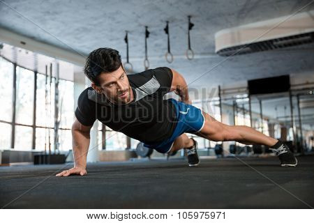 Portrait of a handsome man doing push ups exercise with one hand in fitness gym