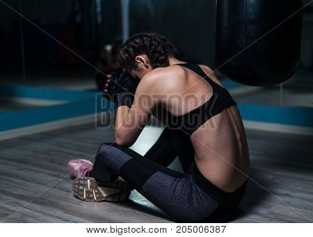 Upset young fighter boxer girl wearing boxing gloves siting on the floor after loosing fight