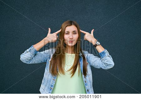 Girl fingers near the temples in the form of pistols, the girl smiles, brunette