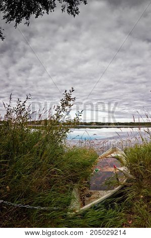 A boat half sunken by a lake in the Northern Finland on an autumn day. It's still chained to a tree although nobody would steal it.