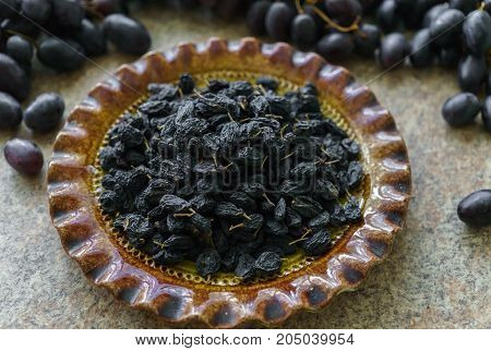 A bunch of fresh sweet dark and succulent raisins poured into a dish grapes lying in a table.