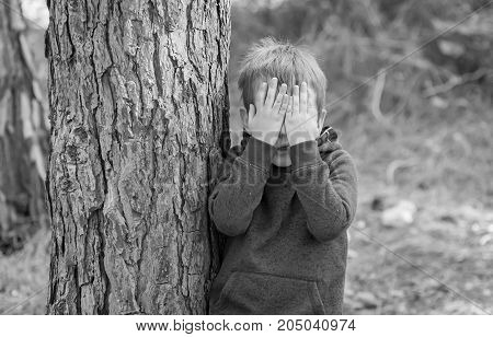 Little Caucasian boy closing his face with hands as if playing hide and seek or scared of something.